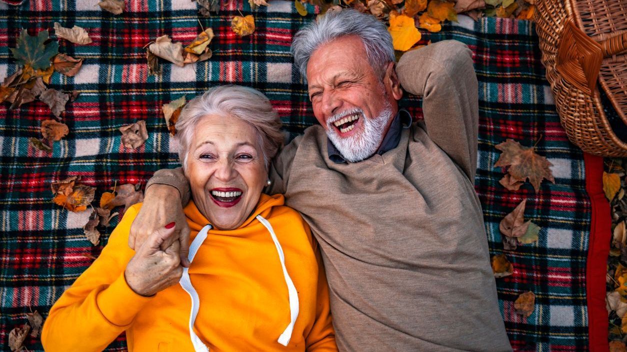 Older couple snuggling and laughing on picnic blanket