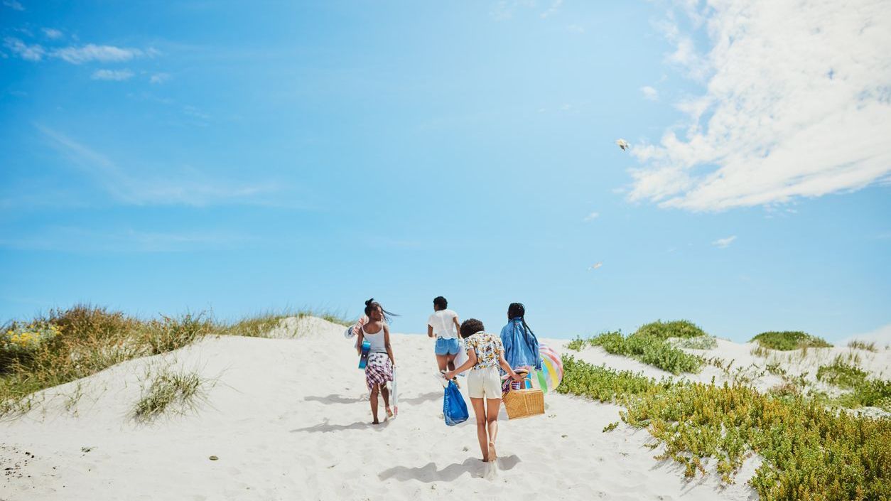 Friends walking up sand dunes with picnic gear