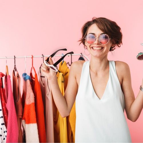 Smiling woman wearing sunglasses posing in front of a hanger full of clothes